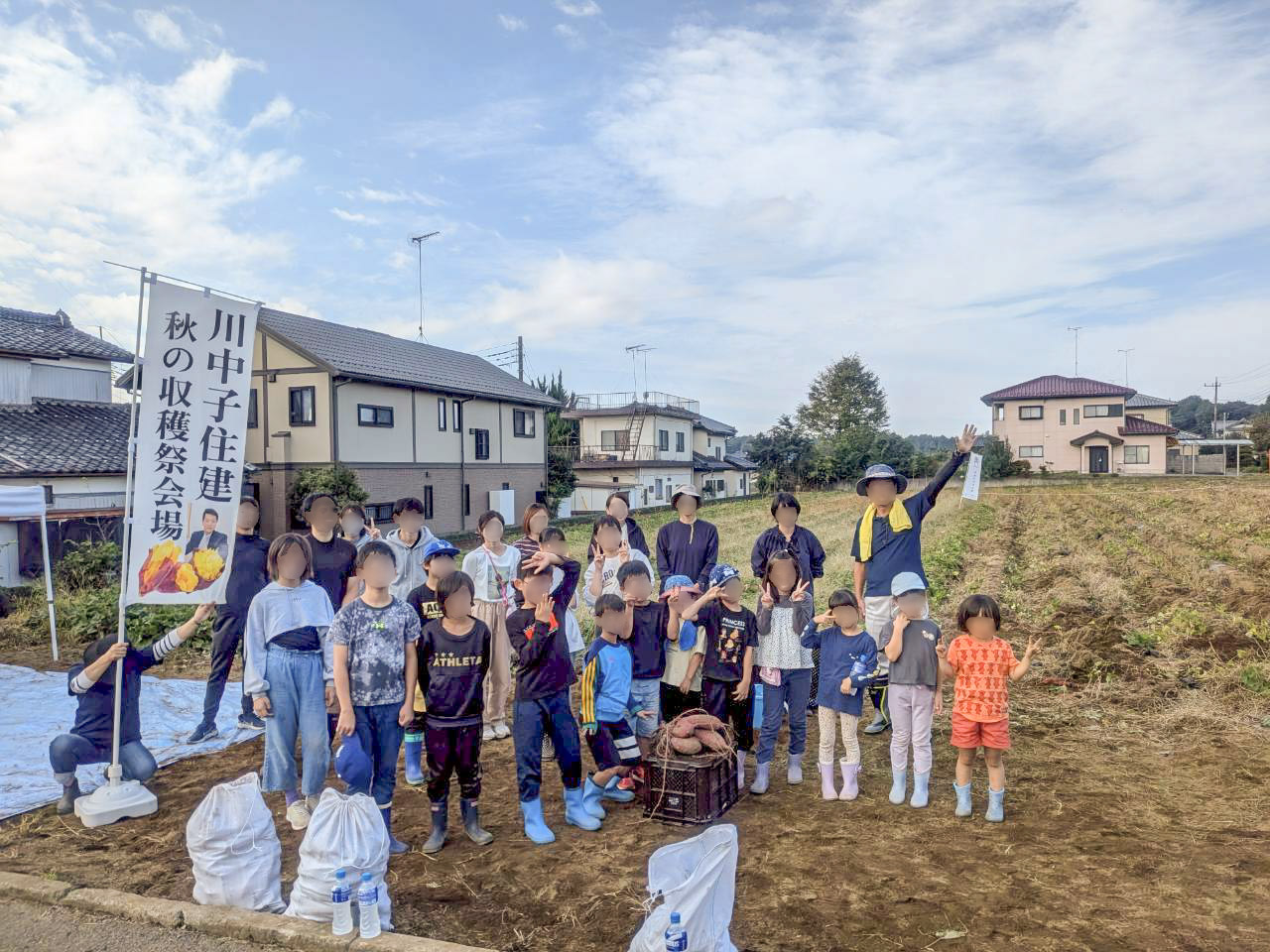 収穫祭ののぼり旗の横で記念撮影をする参加者たち